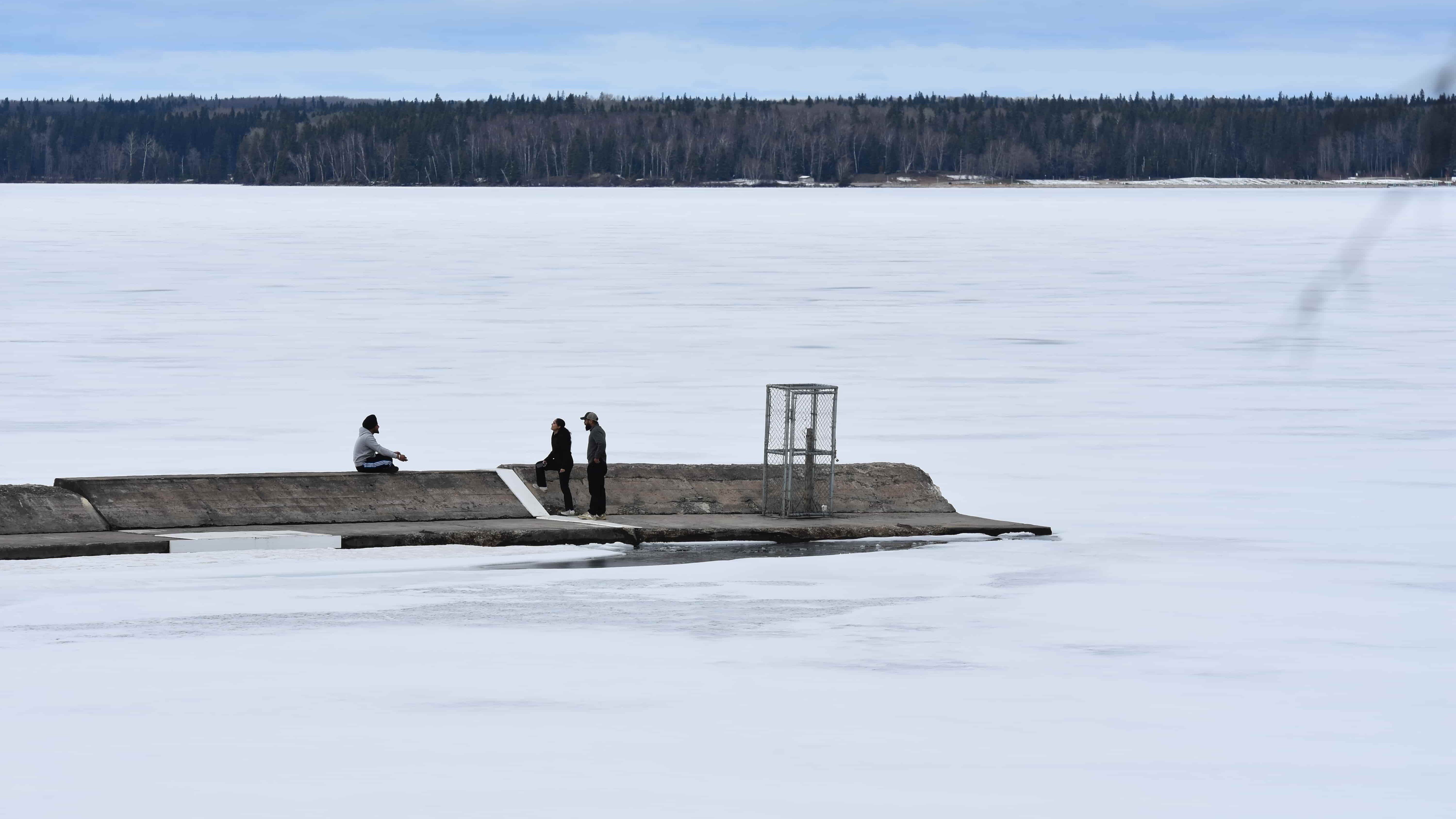 A group of people socialize on the end of the lake's breakwater, surrounded by ice. The concrete structure was built in the 1960s when the marina was located near the townsite, which served as protector to boats and docks at the time.