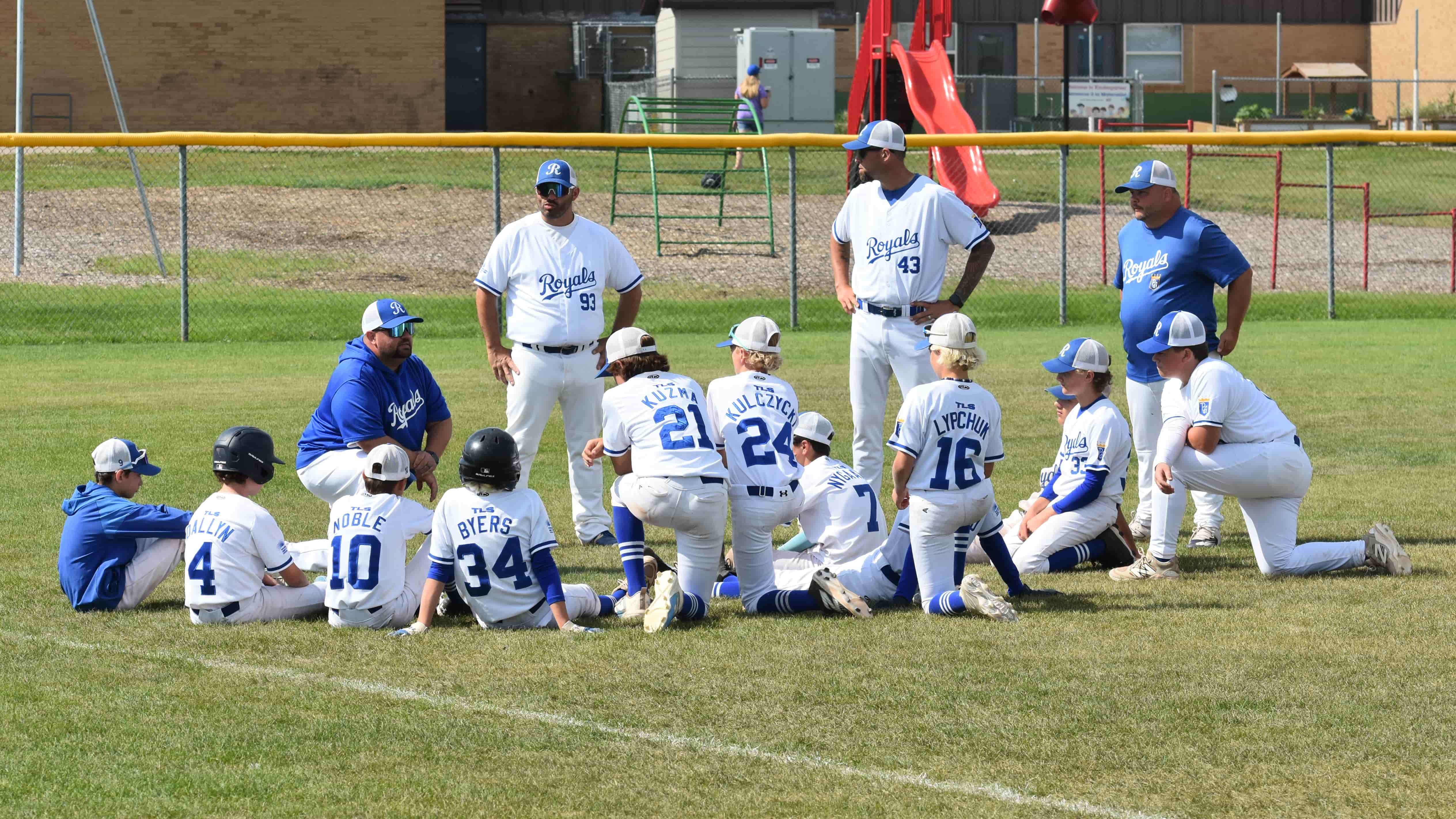 13U Royals coach Tommy Hurd (left) gets down on one knee to talk with his team one last time following the final out of their last game at the AA Western Canadian Baseball Championships.