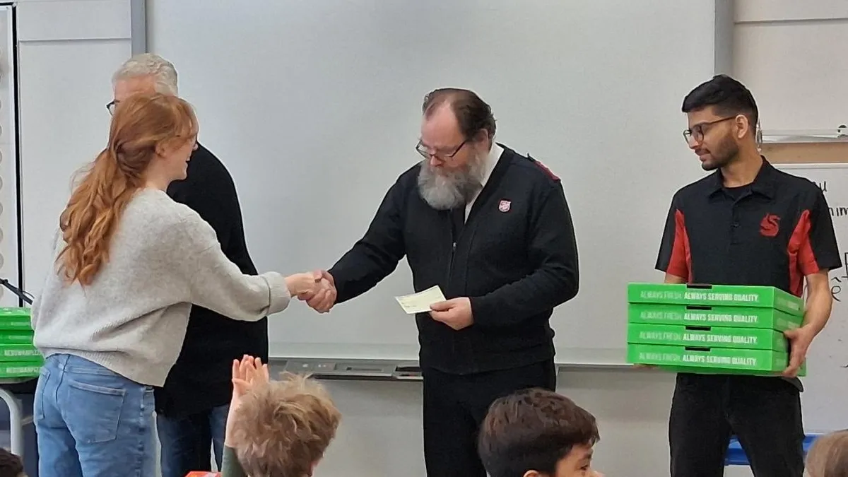 A teacher at École Valois presents Major Ed Dean with a cheque for $1,000.